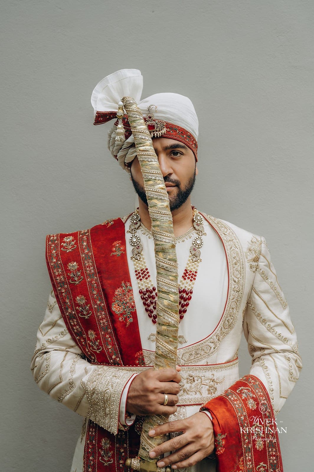 Groom in a cream sherwani with ceremonial sword